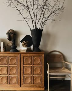 a wooden cabinet sitting next to a chair and vase with branches on top of it