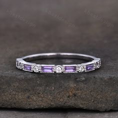 a white gold ring with amethorate and diamonds on top, sitting on a rock