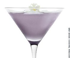 a purple drink in a martini glass with a flower on the rim and white background