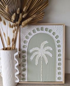 a white vase sitting next to a painting with a palm tree on it's side