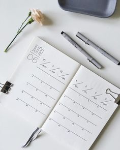 a notepad with writing on it next to some pens and a flower in a vase