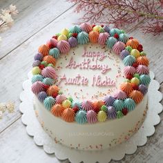 a birthday cake with colorful frosting on a white table next to flowers and branches