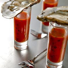 three glasses filled with sauce and oysters on a table next to silver utensils