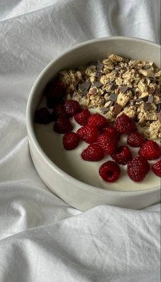 a bowl filled with granola and raspberries on top of a white sheet