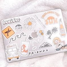 a laptop computer covered in stickers on top of a white blanket with pink and orange accents