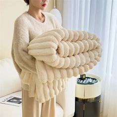 a woman holding a pile of towels in front of a white couch and coffee table