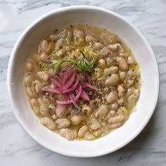 a white bowl filled with beans and garnish on top of a marble table