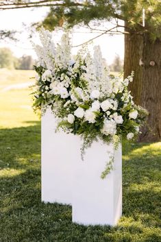 a tall white vase filled with flowers sitting on top of a lush green field next to a tree