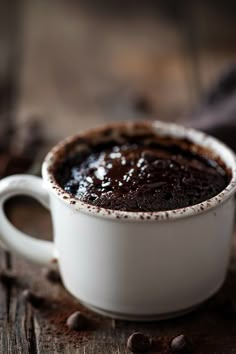 a white cup filled with chocolate pudding on top of a wooden table next to coffee beans