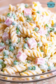 a glass bowl filled with pasta salad on top of a wooden table