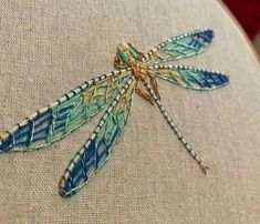 a blue dragonfly sitting on top of a white cloth covered pillow with beading