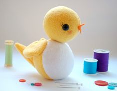 a stuffed bird sitting next to some thread and spools