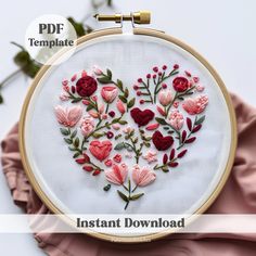 an embroidered heart with flowers and leaves is displayed on a pink cloth next to the embroidery pattern