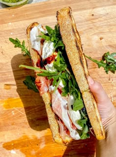 a person holding a sandwich with meat and greens