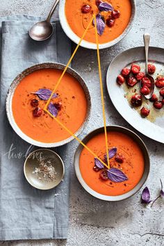 three bowls of carrot soup with garnishes and spoons on the side