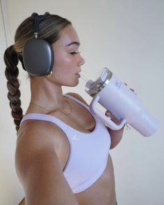 a woman with headphones on drinking out of a cup while holding a blender