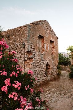 an old stone building with pink flowers in the foreground