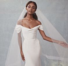 a woman wearing a white wedding dress with a long veil on her head and shoulder