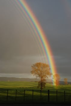 two rainbows in the sky over a green field with trees and a black fence