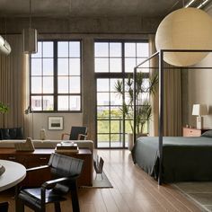 a living room filled with furniture next to large windows and a bed on top of a hard wood floor