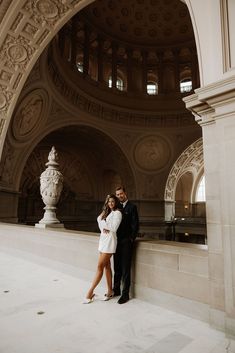 a man and woman standing next to each other in front of a stone building with arches