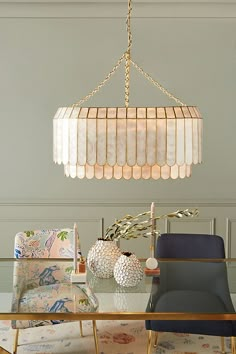 a chandelier hanging over a dining room table with chairs and vases on it