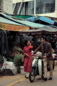 a man and woman riding on the back of a scooter down a street