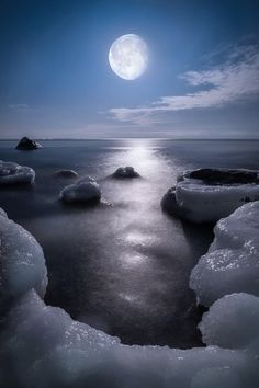 the moon shines brightly in the sky over ice - covered rocks on the water