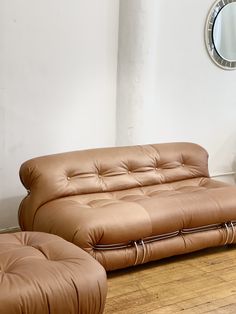 a brown leather couch sitting on top of a hard wood floor next to a mirror