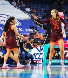 two women in maroon uniforms are on the court and one is holding her hand out