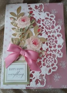 a greeting card with pink flowers and a bow on the front, sitting on top of a doily