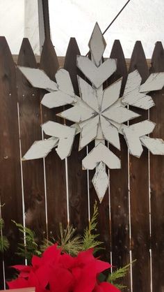 a wooden fence with a snowflake hanging on it's side next to a red poinsetti