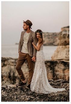 a man and woman standing on rocks near the ocean