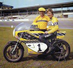 two people sitting on a motorcycle in front of a race track with the number 11