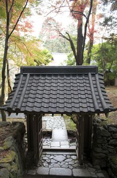 a small pavilion in the middle of a stone path with trees and water behind it