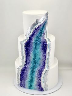 a three tiered cake with blue and purple frosting on the top, sitting on a white plate