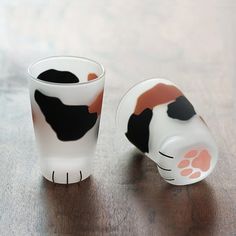 two cups with black and white designs on them sitting on top of a wooden table