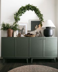 a green cabinet with plants and pictures on the top shelf next to a lamp, mirror and other items