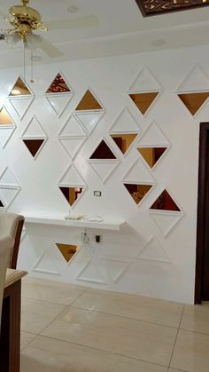 a dining room with white walls and gold geometric shapes on the wall, along with beige chairs