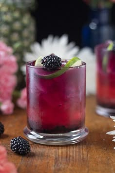 two glasses filled with blackberry lemonade and blackberries on top of a wooden table