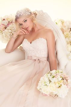 a woman in a wedding dress sitting on a white couch with her hand under her chin