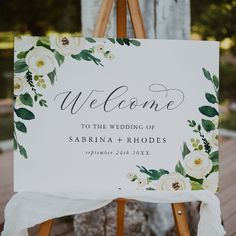 a welcome sign on an easel with flowers and greenery is displayed for the guests