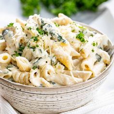 a white bowl filled with pasta and spinach on top of a table next to some parsley