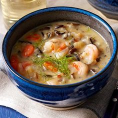 a bowl of soup with shrimp, carrots and mushrooms on a table next to a glass of water