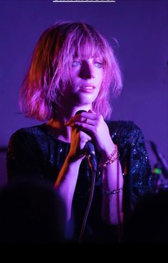 a woman with pink hair holding a microphone in front of her face and looking off to the side