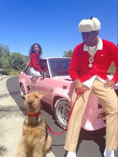 a man sitting on the back of a pink car next to a woman with a dog