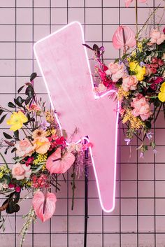 a pink neon sign sitting on top of a table next to flowers and greenery