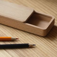 two pencils are sitting next to a wooden box on a table with a pen in it