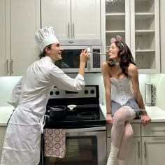 a man and woman dressed up as chefs in the kitchen, one is holding a spoon