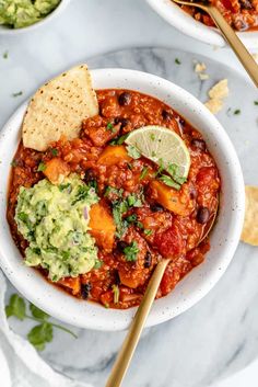 two bowls filled with chili and guacamole next to tortilla chips